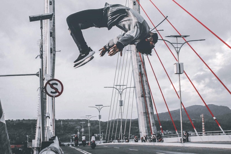 Un acróbata dando un salto mortal hacia atrás encima de un puente